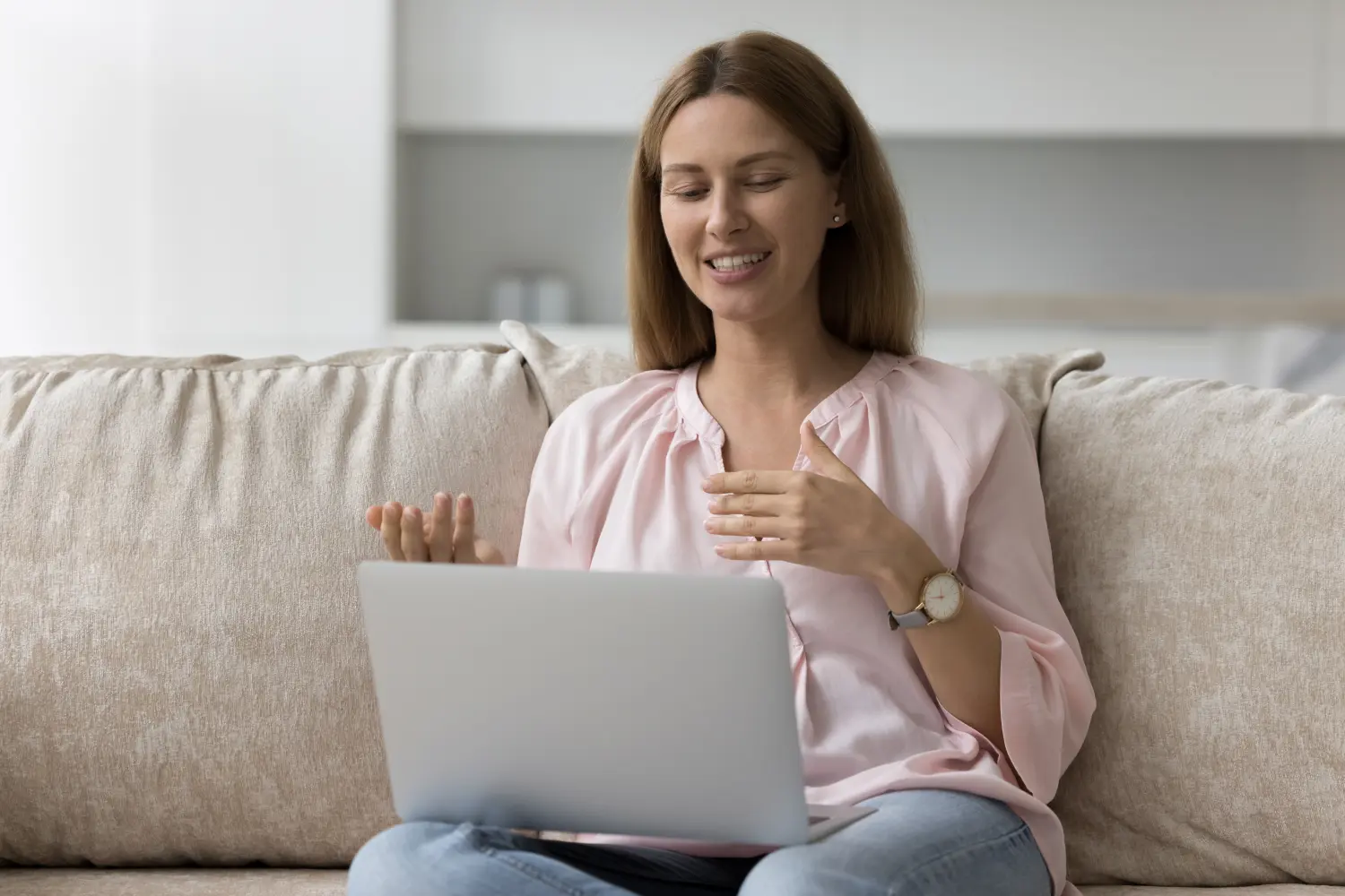 Eine Millennial-Frau aus den 30er-Jahren spricht über eine Videokonferenzanwendung, sitzt mit einem Laptop auf dem Sofa und hat eine angenehme Kommunikation